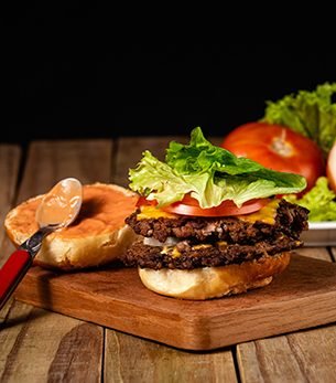 A vertical shot of a delicious hamburger with the sauce of the bread on a wooden board